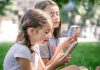 Duas meninas usam celular em área verde ao ar livre