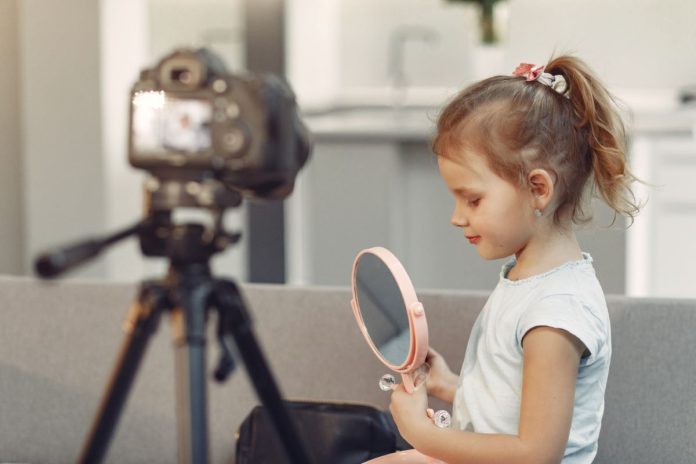 Menina maquiada se olha no espelho em frente a câmera de vídeo