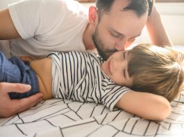 Pai beija no rosto o filho, que está deitado na cama