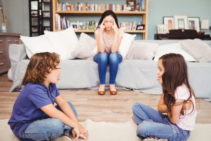 Irmãos brigam na sala de casa na frente da mãe cansada