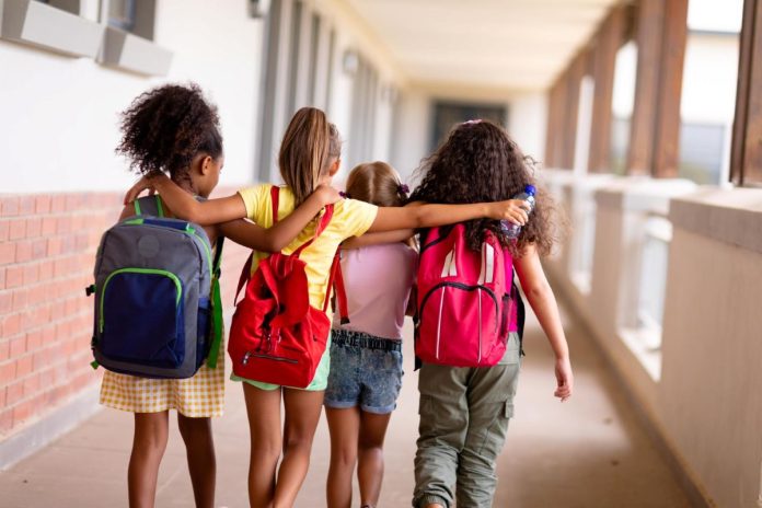 Crianças caminham de braços dados em corredor da escola