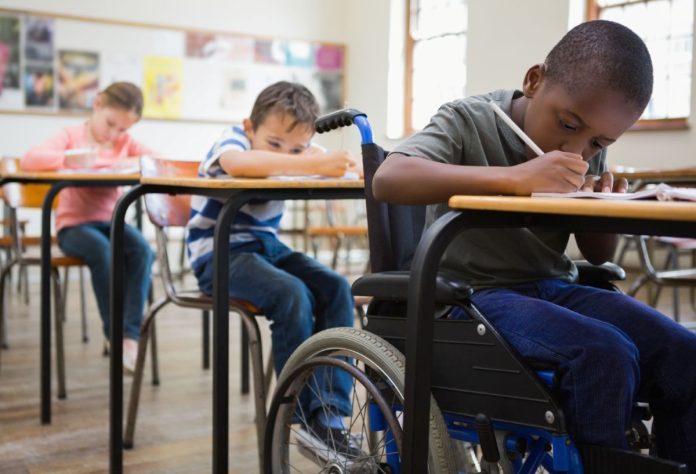 Aluno cadeirante escreve em caderno na sala de aula