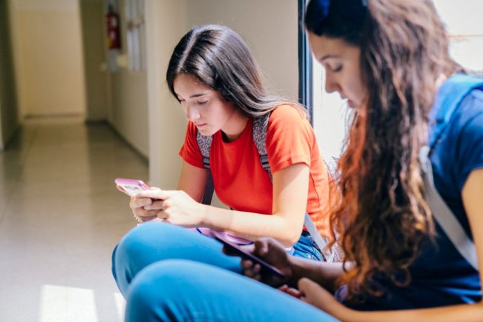 Adolescentes não têm apoio para lidar com as redes sociais, diz estudo Duas adolescentes acessam redes sociais no celular